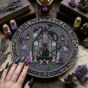 magical fantasy cross-stitch pattern featuring a black cat sitting inside a gothic greenhouse while a dark dragon with green wings curls protectively around the roof. The scene is decorated with lavender flowers, leafy vines, purple crystals, potion bottles, hanging lanterns, crescent moon charms, and celestial ornaments. The rich palette of black, green, lavender, gray, purple, and gold creates a mystical witchy garden mood, perfect for cat lovers, dragon fans, fantasy décor, and handmade walL