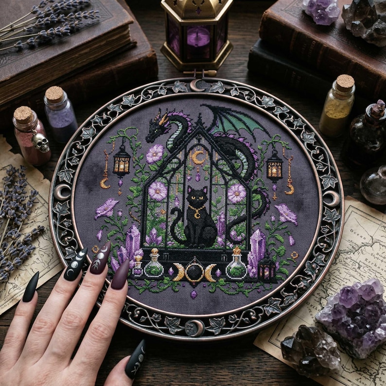 magical fantasy cross-stitch pattern featuring a black cat sitting inside a gothic greenhouse while a dark dragon with green wings curls protectively around the roof. The scene is decorated with lavender flowers, leafy vines, purple crystals, potion bottles, hanging lanterns, crescent moon charms, and celestial ornaments. The rich palette of black, green, lavender, gray, purple, and gold creates a mystical witchy garden mood, perfect for cat lovers, dragon fans, fantasy décor, and handmade walL