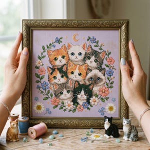 May include: Framed cross-stitch artwork featuring a group of adorable cats surrounded by flowers and greenery. The artwork is set against a lavender background with a crescent moon. The frame is ornate and gold-colored.