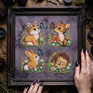 May include: Framed cross-stitch art featuring four woodland creatures: a fox, deer, rabbit, and hedgehog. Each animal is surrounded by flowers and butterflies. The artwork is in a dark, ornate frame, with a wooden background.