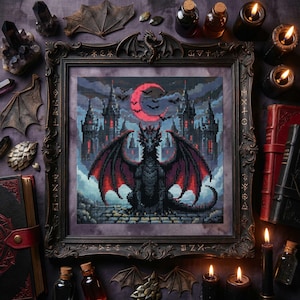 May include: Framed cross-stitch art featuring a black dragon with red-tipped wings, set against a gothic castle under a red moon. The artwork is surrounded by candles, books, and decorative elements, creating a dark fantasy theme.