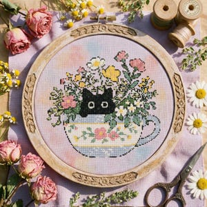 Peut inclure: Broderie au point de croix d'un chat noir dans une tasse à thé fleurie, encadrée dans un cercle en bois. L'image présente des roses séchées, des marguerites et des ciseaux anciens. La tasse à thé est ornée de motifs floraux.