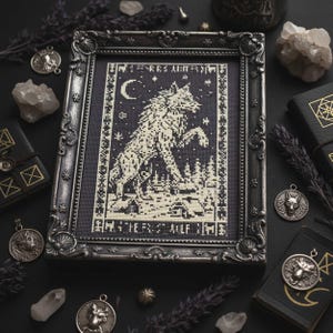 May include: Framed cross-stitch art featuring a wolf leaping in a forest under a crescent moon and stars. The artwork is in black and cream colors, with the text "THE FIRST WOLF TIME" at the bottom. The frame is ornate, dark gray, and surrounded by other gothic-themed items.