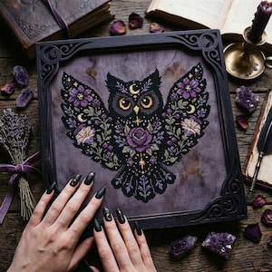 May include: A square cross-stitch embroidery featuring a black owl with yellow eyes, surrounded by purple flowers, vines, and golden crescent moon symbols. The artwork is displayed in a dark, ornate wooden frame on a textured purple fabric background.