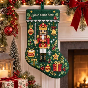 Op de afbeelding: Een donkergroene kerstkous met naaldwerk, voorzien van een centrale notenkraker met een zwaard, omringd door motieven van een trommel, ster, bel en cadeaus. De bovenrand toont de tekst your name here in witte letters.