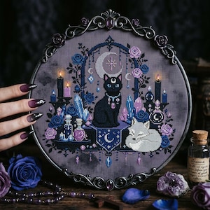 Puede incluir: Un bastidor de bordado circular con un diseño de punto de cruz de un gato negro y un zorro blanco rodeados de rosas azules y moradas, cristales, velas y una luna creciente sobre tela gris oscuro con un marco de metal ornamentado.
