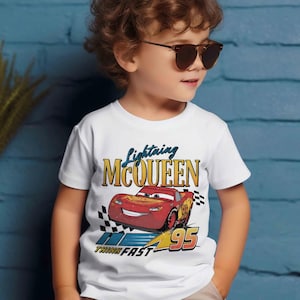 May include: White t-shirt featuring Lightning McQueen from the Cars movie. The graphic includes the car, the number 95, and the words "Lightning McQueen" and "Think Fast". The shirt is worn by a young child wearing sunglasses.