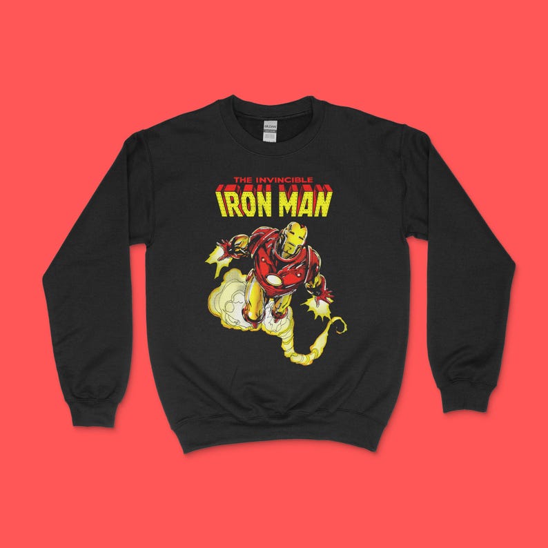May include: A black long-sleeve sweatshirt featuring a graphic print of the character Iron Man in a red and gold suit, flying with yellow exhaust trails. Above the character, the text reads THE INVINCIBLE IRON MAN in yellow and red block letters.