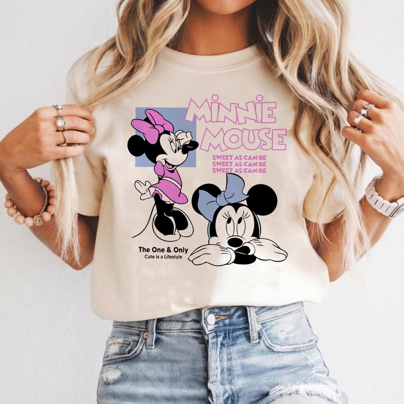 Puede incluir: Camiseta color crema con un gr&aacute;fico de Minnie Mouse. El dise&ntilde;o incluye dos ilustraciones de Minnie Mouse, el texto "MINNIE MOUSE" y la frase "SWEET AS CAN BE". Tambi&eacute;n est&aacute; presente el texto "The One & Only Cute is a Lifestyle".