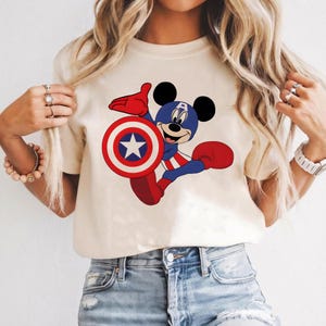 Peut inclure: T-shirt cr&egrave;me avec Mickey Mouse en dessin anim&eacute;, d&eacute;guis&eacute; en Captain America. Mickey tient un bouclier avec une &eacute;toile blanche et porte un costume bleu et rouge. Le t-shirt a un col rond et des manches courtes.