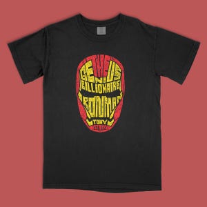May include: A black short-sleeve t-shirt featuring a graphic of a helmet shape formed by yellow text on a red background. The text reads: THE GENIUS BILLIONAIRE IRON MAN TONY STARK. The graphic has a distressed, weathered texture throughout the design.