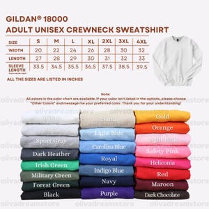 May include: A Gildan 18000 adult unisex crewneck sweatshirt size chart with measurements in inches, featuring a white sweatshirt image and a color palette display showing various folded fabric options including white, sand, gold, ash, light blue, orange, sport gray, carolina blue, light pink, dark heather, royal, safety pink, irish green, indigo blue, heliconia, military green, navy, red, forest green, purple, maroon, black, and dark chocolate.