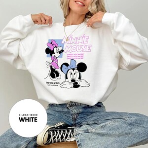 Puede incluir: Sudadera blanca con un gr&aacute;fico de Minnie Mouse. El dise&ntilde;o incluye dos ilustraciones de Minnie Mouse, el texto "Minnie Mouse" y la frase "Sweet as can be". La sudadera es una Gildan 18000 en blanco.