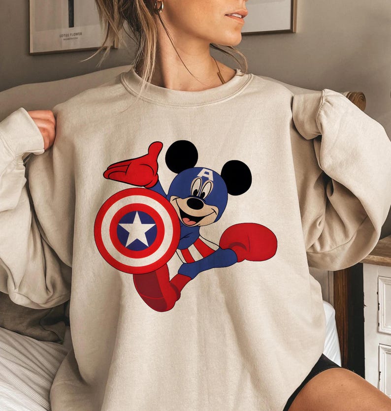 Peut inclure: Sweat-shirt beige avec Mickey Mouse en Captain America. Mickey porte un casque bleu avec un "A" blanc, des gants et des bottes rouges, et tient un bouclier avec une &eacute;toile blanche. Le design est rouge, blanc et bleu.