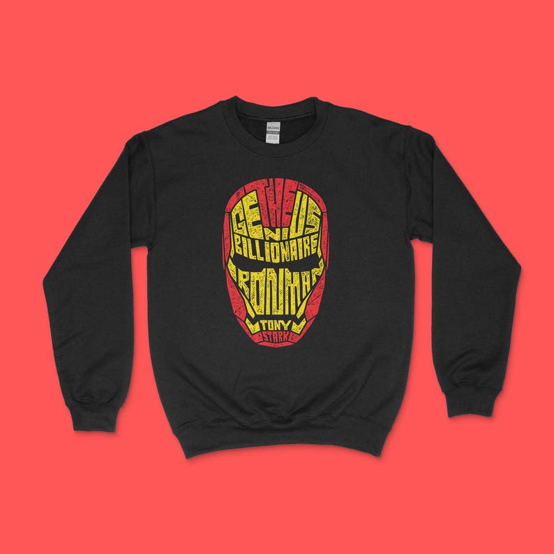 May include: A black long-sleeve sweatshirt featuring a graphic of a mask in red and yellow. The mask is composed of the text "GENIUS BILLIONAIRE PLAYBOY PHILANTHROPIST" and "IRON MAN TONY STARK" arranged to form the shape of the iconic superhero helmet.