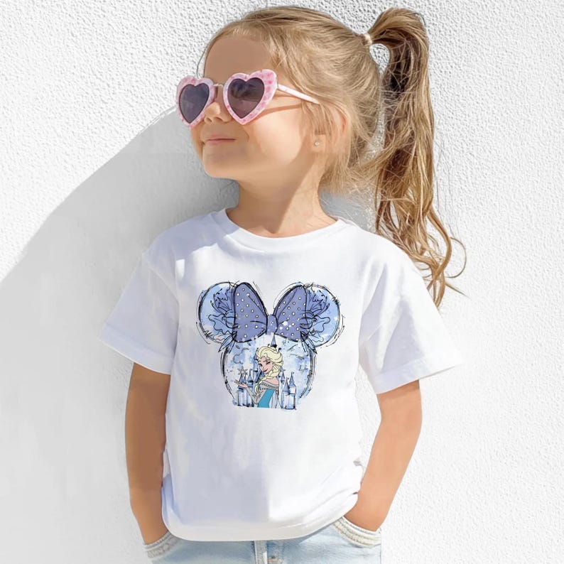 May include: A white t-shirt featuring a cartoon design of a princess with a blue bow and mouse ears. The girl is wearing pink heart-shaped sunglasses. The shirt is short-sleeved and made of a soft material.