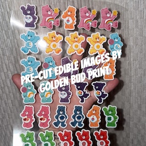 May include: A sheet of pre-cut edible images featuring colorful Care Bears. The bears are in various colors, including pink, blue, orange, and purple. Text on the sheet reads "PRE-CUT EDIBLE IMAGES BY GOLDEN BUD PRINT."