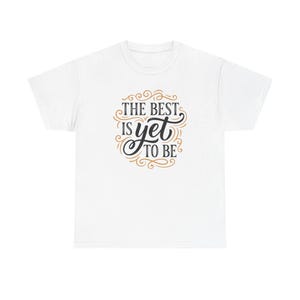 May include: White t-shirt featuring the quote "THE BEST IS YET TO BE" in black and gold script. The design uses elegant, swirling typography, making it a stylish and inspirational apparel item.