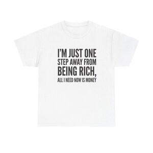 May include: White t-shirt with the text "I'M JUST ONE STEP AWAY FROM BEING RICH, ALL I NEED NOW IS MONEY" in black. The shirt is a casual wear item, suitable for everyday use.