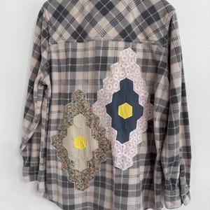 Peut inclure: Une chemise à manches longues boutonnée avec un motif à carreaux beige et gris anthracite. Le dos présente deux grandes pièces rapportées en forme de losange composées d'hexagones en tissu floral, gris uni et jaune.