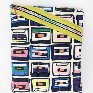 May include: A yellow zippered pouch with a quilted design. The pouch is covered in a print of colorful cassette tapes.