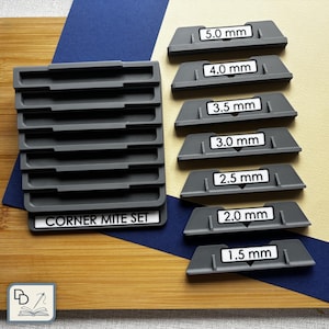 Puede incluir: Un juego de ingletes grises con medidas de 1,5 mm a 5,0 mm. El juego incluye varias piezas, cada una etiquetada con un tamaño específico en milímetros. El texto "CORNER MITE SET" es visible en una pieza.