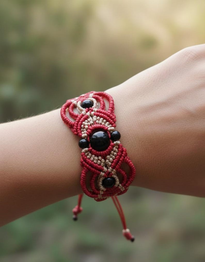 May include: A red and beige macrame bracelet with black beads. The bracelet has a woven design with a central pattern of black beads and a red cord. The bracelet is tied with a red cord.