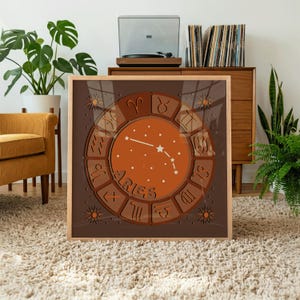 May include: A square framed wall art print featuring a dark brown background with a central orange circular zodiac wheel. The wheel displays twelve astrological symbols and the word Aries in stylized text, surrounding a constellation of white stars.