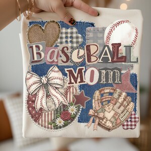May include: Cream-colored baseball mom t-shirt with a patchwork design. Features a baseball, bow, glove, and heart. The words "Baseball Mom" are prominently displayed in a mix of fonts and colors. The design incorporates denim, floral, and star elements.