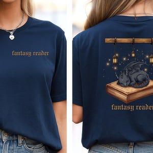 Könnte beinhalten: Marineblaues T-Shirt mit dem Aufdruck "fantasy reader" auf der Vorderseite. Auf der Rückseite ist ein schlafender schwarzer Drache auf einem Buch abgebildet, mit Laternen und dem Schriftzug "fantasy reader".