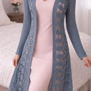 Puede incluir: Cárdigan largo de crochet azul con detalles florales. El cárdigan es largo hasta la rodilla y tiene mangas largas. La prenda se lleva sobre un vestido rosa. El fondo incluye una cama y una mesita de noche con flores.