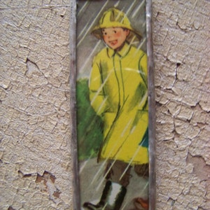 Puede incluir: Una imagen enmarcada de un ni&ntilde;o con un impermeable amarillo y un sombrero caminando bajo la lluvia. La imagen est&aacute; enmarcada en plata.