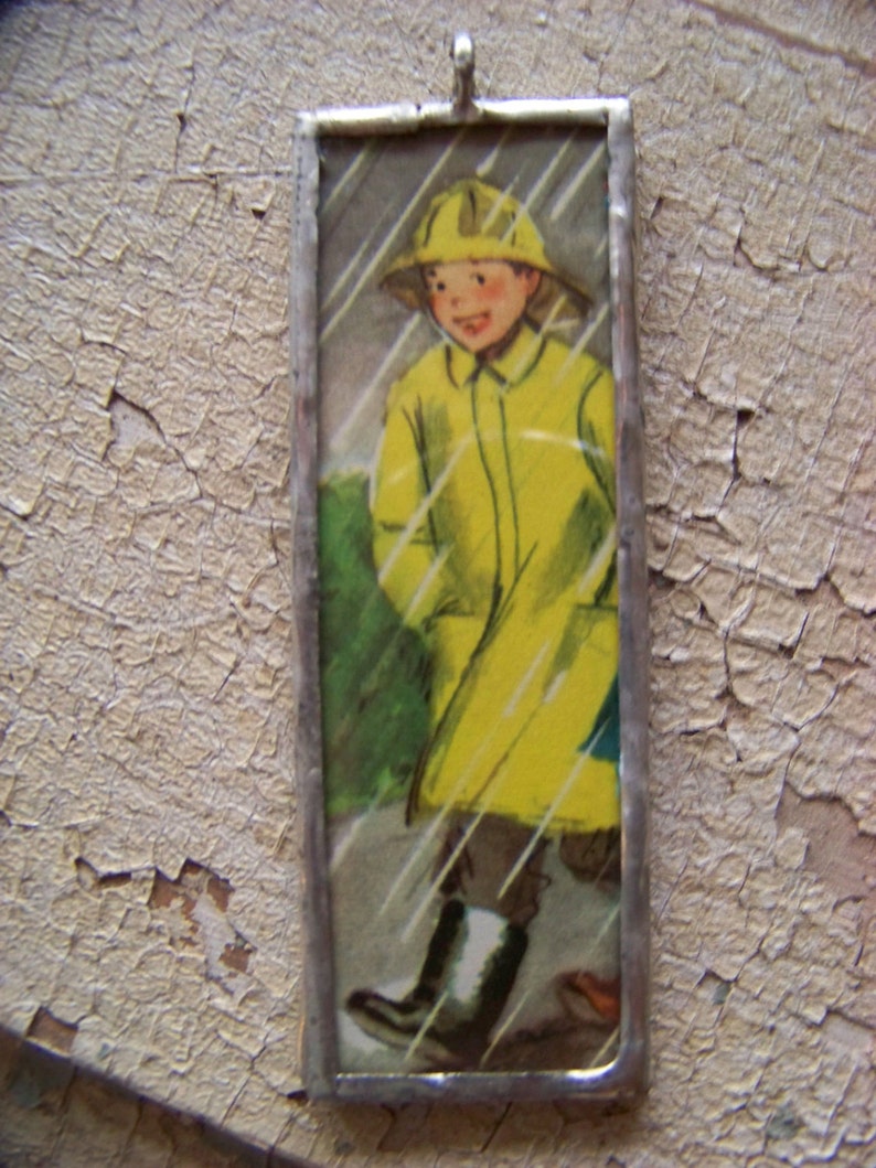 Puede incluir: Una imagen enmarcada de un ni&ntilde;o con un impermeable amarillo y un sombrero caminando bajo la lluvia. La imagen est&aacute; enmarcada en plata.