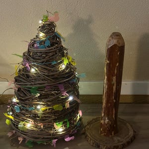 May include: A decorative, handcrafted tree made of woven brown branches, adorned with colorful leaf-shaped accents and small white lights. Beside it is a wooden candle holder with a natural wood grain finish, set on a round wooden base.
