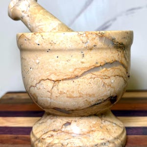 May include: A white ceramic mug with a black handle and the text "But First, Coffee" in a bold, black font. The mug is set against a neutral background, highlighting its simple design.