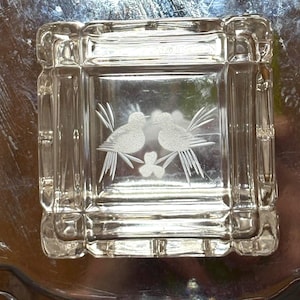 May include: A clear, square glass dish with etched bird and clover designs. The dish has a decorative border and is likely used for serving or display. The etched details add a touch of elegance to the piece.