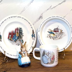 May include: A collection of Peter Rabbit themed items, including two white plates with illustrations and text, a ceramic mug, and a rabbit figurine. The plates and mug feature scenes from the story.