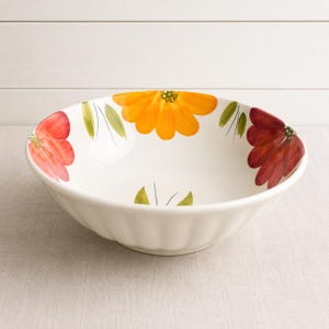 May include: A white ceramic serving bowl with a fluted exterior and a hand-painted floral pattern on the interior rim. The design features large, vibrant orange, red, and deep burgundy flower petals interspersed with green leaves and thin stems.