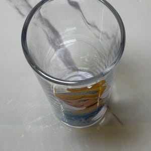 May include: A clear glass tumbler featuring a cartoon image of Cinderella. The glass has a cylindrical shape and a thick rim. The image of Cinderella is in the lower portion of the glass, with her face and upper body visible.