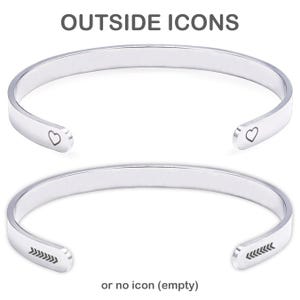 May include: Two silver-toned metal cuff bracelets. The top bracelet features a small heart icon engraved on each end. The bottom bracelet features a series of five small arrows engraved on each end. The text OUTSIDE ICONS and or no icon (empty) appears.