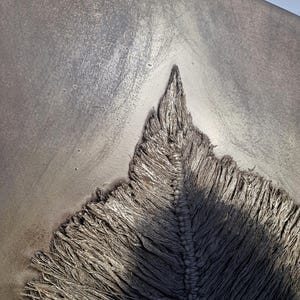 May include: Close-up of a textured, gray artwork with a central, pointed design. The artwork features a rough, frayed texture, with a central ridge and a gradient of light and shadow.