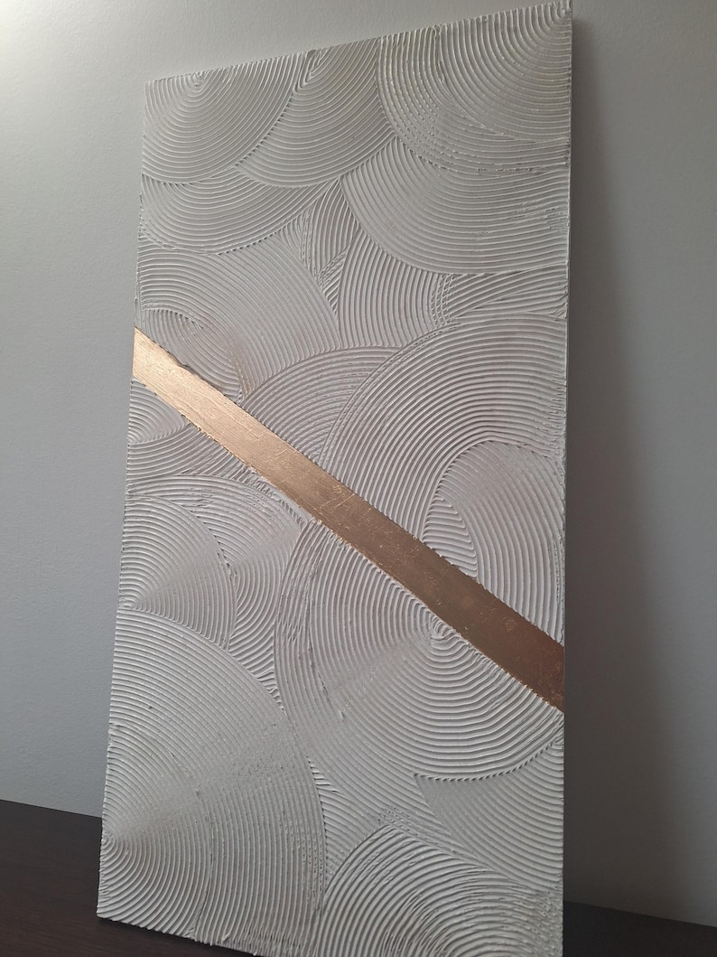 May include: Textured white rectangular wall art with a repeating circular pattern and a diagonal gold stripe. The artwork has a raised, tactile surface, creating depth and visual interest. The piece is displayed against a neutral background.