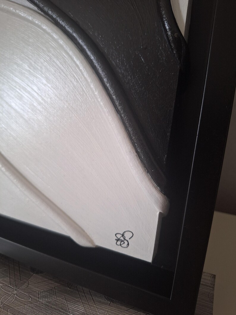 May include: Abstract framed artwork with a textured surface. The piece features a contrast of black and white, with a signature in the lower right corner. The artwork is encased in a black frame.