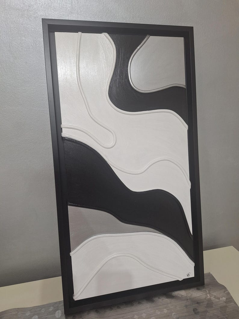 May include: Abstract wall art in a black frame. The artwork features a layered design with flowing shapes in black, white, and gray. The piece has a textured appearance, adding depth and visual interest to the modern design.