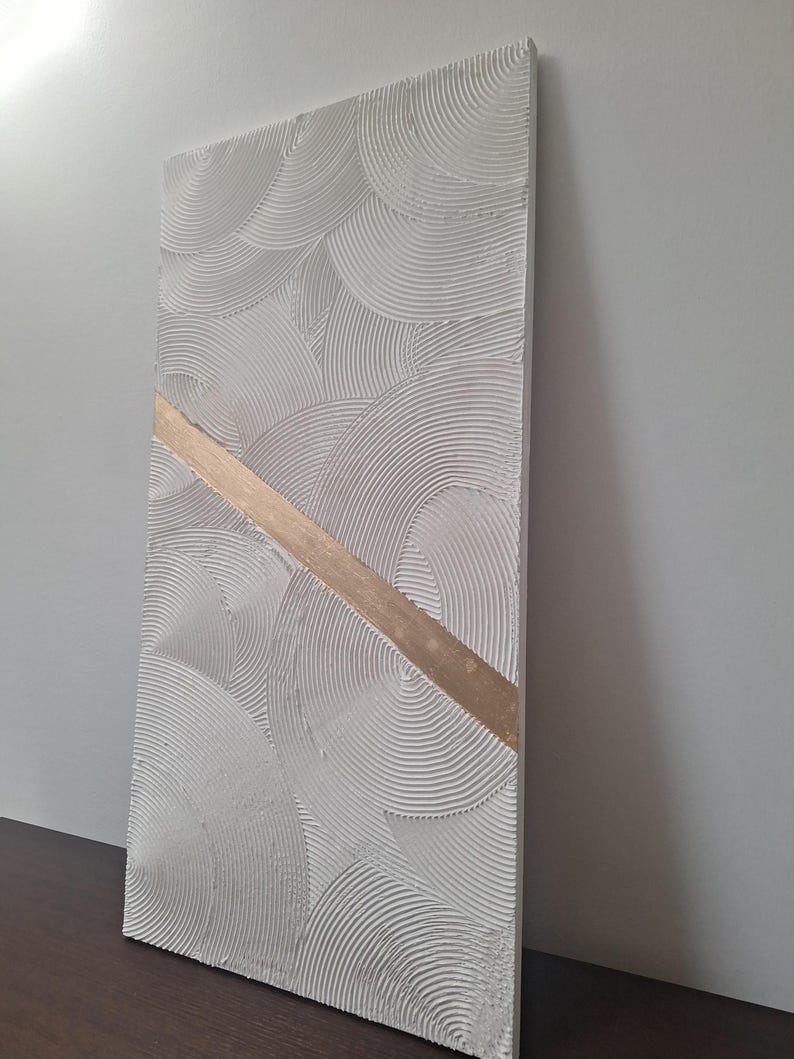 May include: Textured white rectangular wall art with a repeating semi-circular pattern. A diagonal gold-colored stripe bisects the artwork. The piece is displayed against a neutral background, showcasing its three-dimensional texture.
