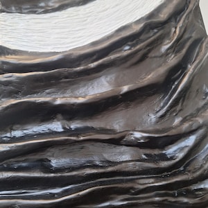 May include: Abstract sculpture with a textured surface. The artwork features flowing, wave-like forms in glossy black, contrasted by a white, textured section. The piece has a dynamic, organic feel.