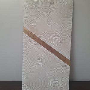 May include: Rectangular textured white artwork with a repeating circular pattern. A diagonal gold-colored stripe bisects the artwork. The piece is displayed against a neutral background, showcasing its minimalist design.