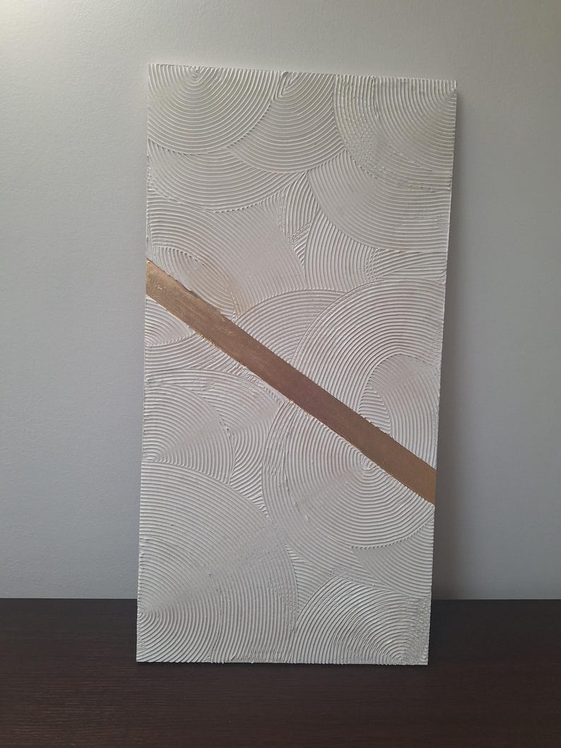 May include: Rectangular textured white artwork with a repeating circular pattern. A diagonal gold-colored stripe bisects the artwork. The piece is displayed against a neutral background, showcasing its minimalist design.
