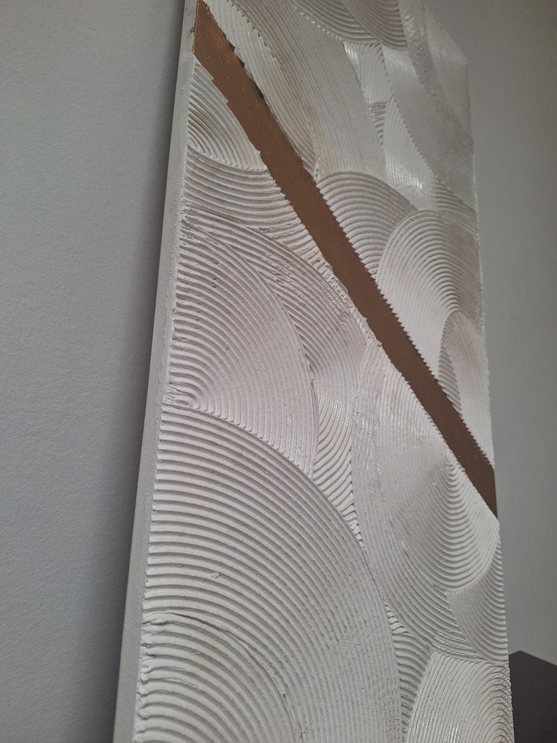May include: Textured white wall art with a diagonal brown stripe. The artwork features a repeating pattern of semi-circular, ridged designs. The piece is mounted on a rectangular wooden frame, creating a modern, abstract aesthetic.