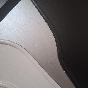 May include: Close-up of a painted surface with a curved design. The color scheme includes white, silver, gray, and black. The paint has a textured appearance, with visible brushstrokes.
